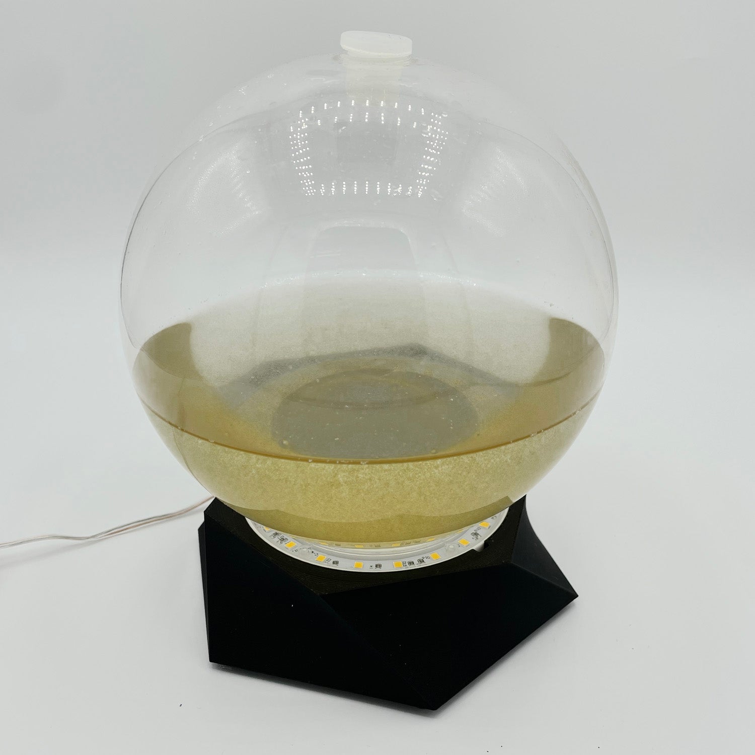 A bioluminescent glass bio-orb on a grow light - a micro-aquarium with living algae.